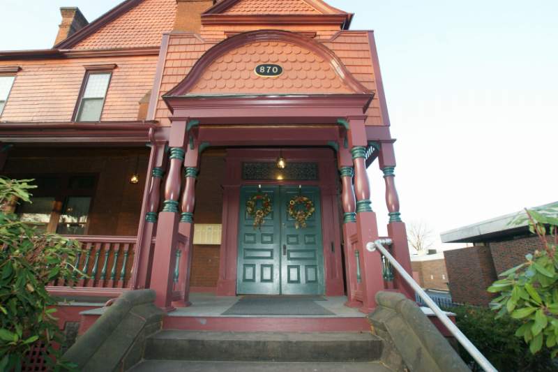 The carved front porch and green double doors of 870 West Fourth Street